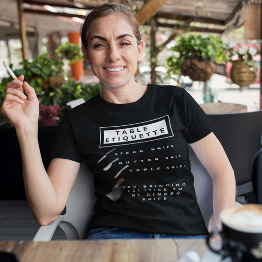 Woman wearing a black t-shirt with 'Table Etiquette' text, sitting at an outdoor cafe.