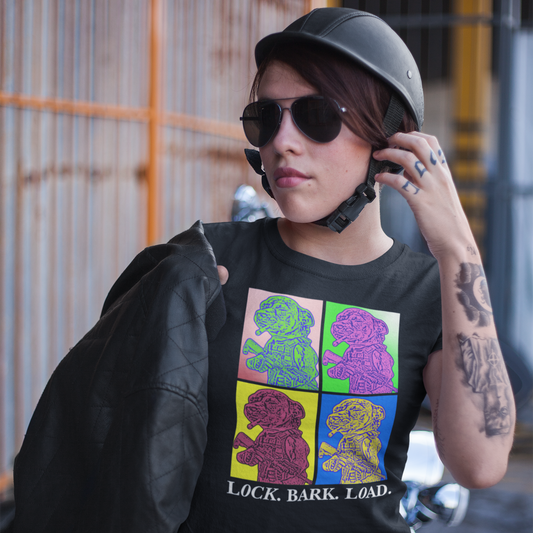 A woman wearing a half helmet style motorcycle helmet and mirrored sunglass, standing outdoors in an urban setting, holding a black leather jacket to her shoulder with her right hand. She is wearing a black women's t-shirt with a four-panel pop-art graphic of the tactical Chihuahua meme, with the text 'Lock. Bark. Load' underneath as a tribute to the New Order album 'Technique' pop art style cover art. Her left tattoo covered arm and hand are reaching to her left ear.