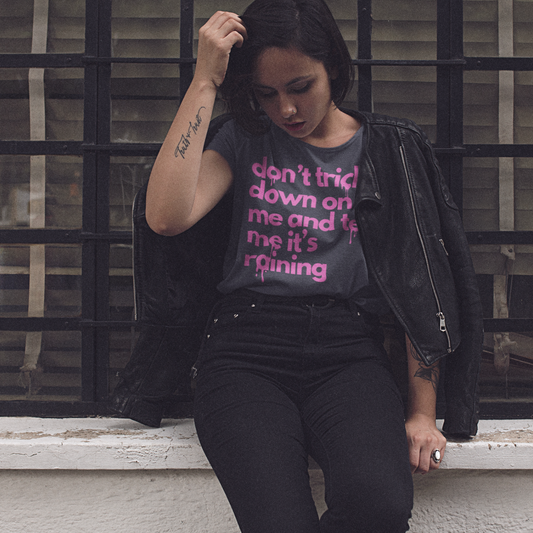 Woman wearing a black jacket and graphic t-shirt sitting on a ledge with a window in the background