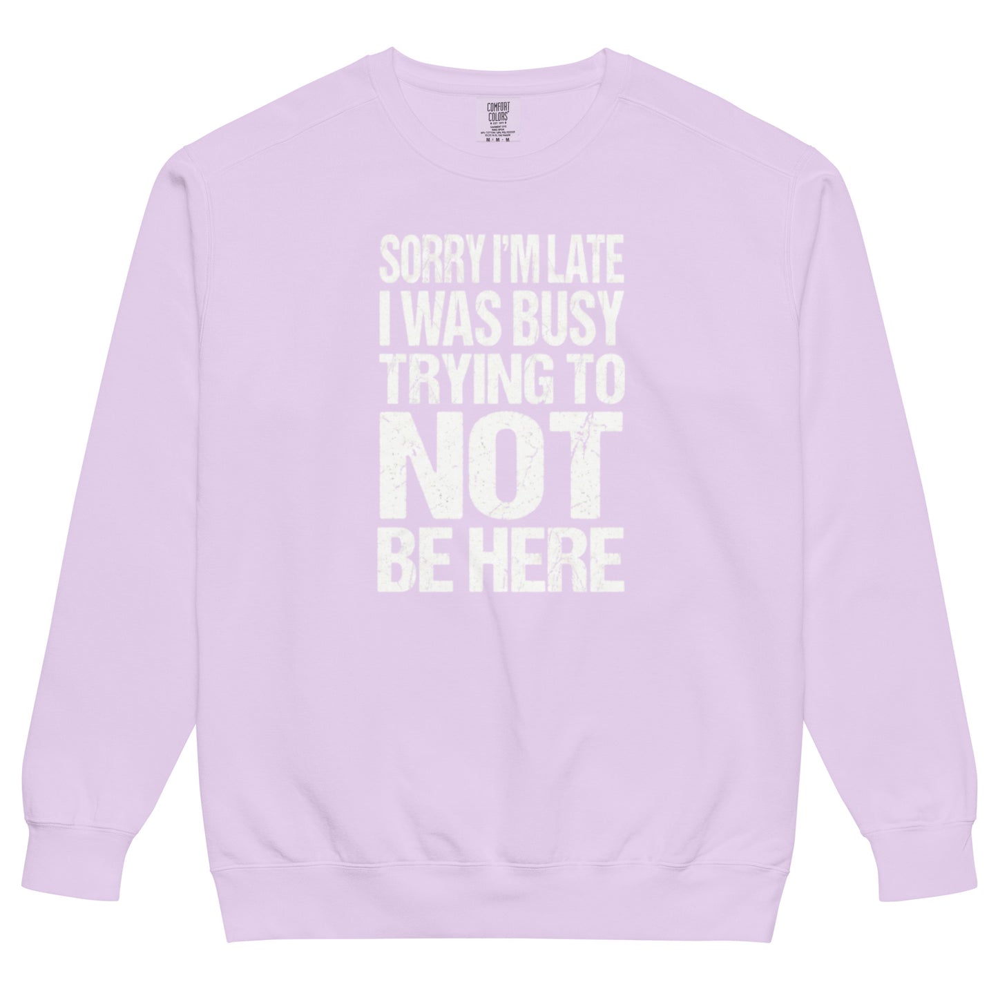 An orchid colored sweatshirt with an all-caps, distressed, white text graphic reading "SORRY I'M LATE I WAS BUSY TRYING TO NOT BE HERE" stacked in a rectangle on the chest.