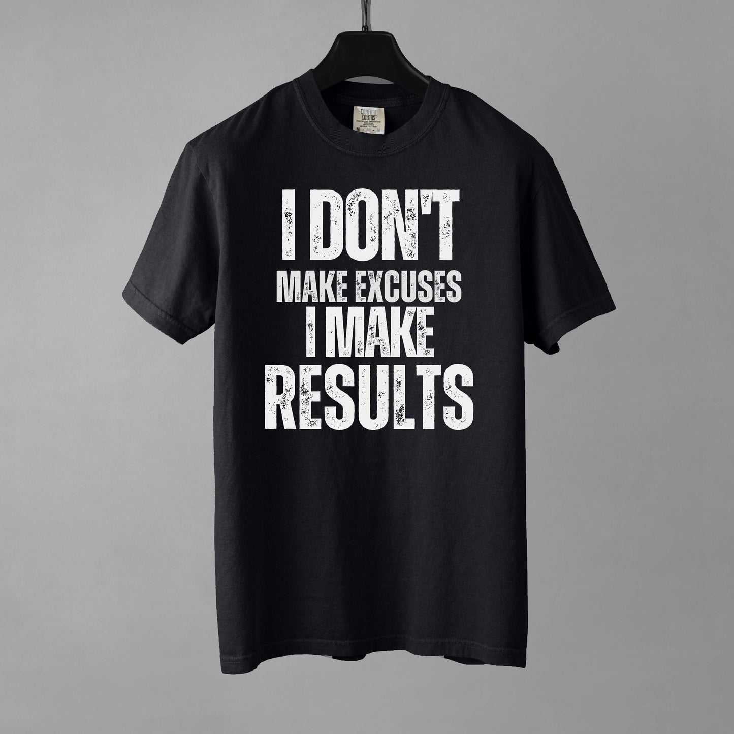 A black t-shirt with bold, all-caps, distressed text that reads 'I DON'T MAKE EXCUSES I MAKE RESULTS', on a gray background.