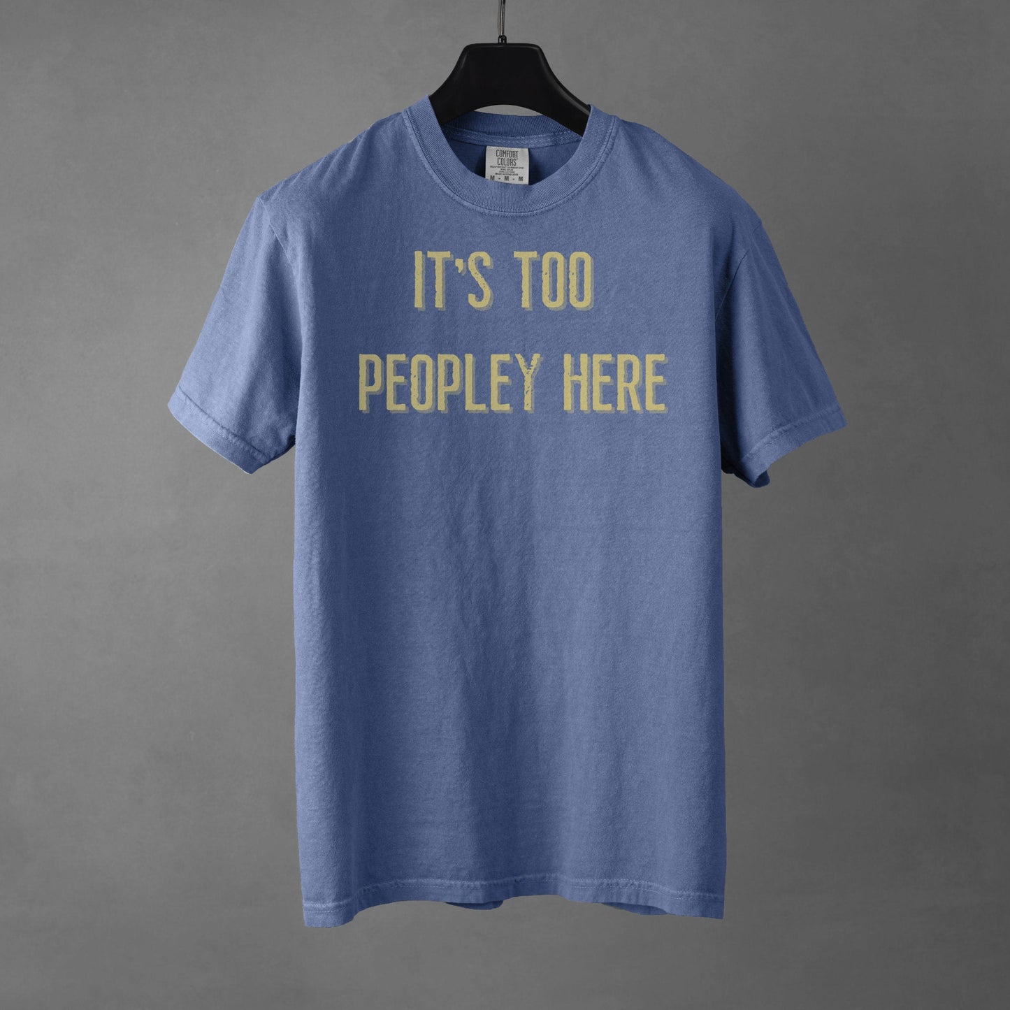 Blue t-shirt with yellow text 'IT'S TOO PEOPLEY HERE' on a gray background