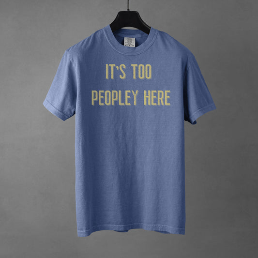 Blue t-shirt with yellow text 'IT'S TOO PEOPLEY HERE' on a gray background