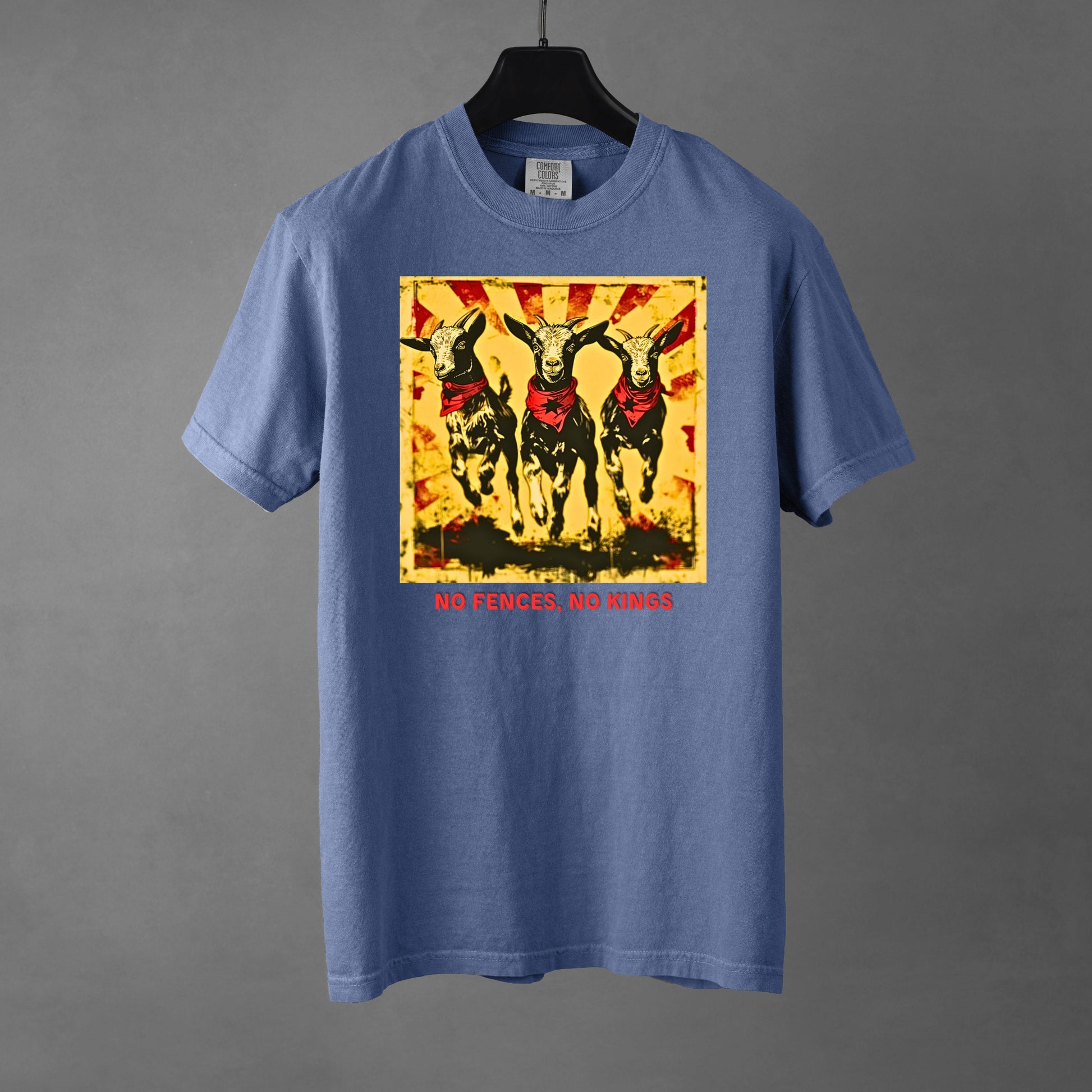 A blue jean colored Comfort Colors 1717 heavyweight t-shirt featuring a "No Fences, No Kings" graphic with three goats in red bandanas and a distressed sunburst background. Below the graphic is bold, red, all-caps text that reads, "NO FENCES, NO KINGS". The garment rests on a black hanger against a gradient gray background. 