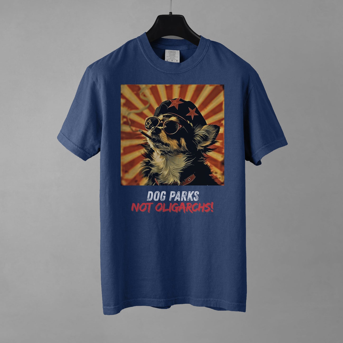A denim colored men's t-shirt with a graphic of a Chihuahua wearing sunglasses and a beret against a 50's style propaganda background with bold all-caps text underneath that reads "DOG PARKS NOT OLIGARCHS".