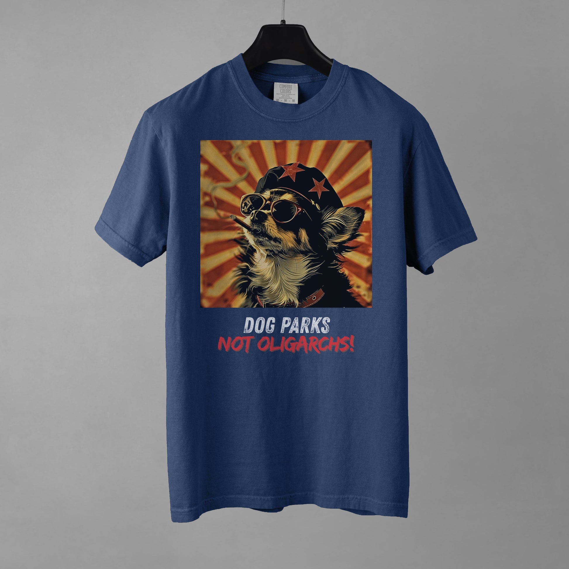 A denim colored men's t-shirt with a graphic of a Chihuahua wearing sunglasses and a beret against a 50's style propaganda background with bold all-caps text underneath that reads "DOG PARKS NOT OLIGARCHS".
