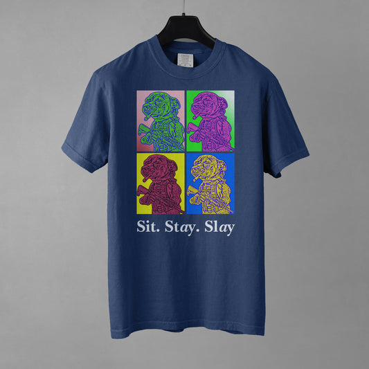 A true navy colored women's t-shirt with a four-panel pop-art graphic of the tactical Chihuahua meme, with the text 'Sit. Stay. Slay' underneath as a tribute to the New Order album 'Technique' pop art style cover art. The t-shirt is on a black hanger against a gray background.