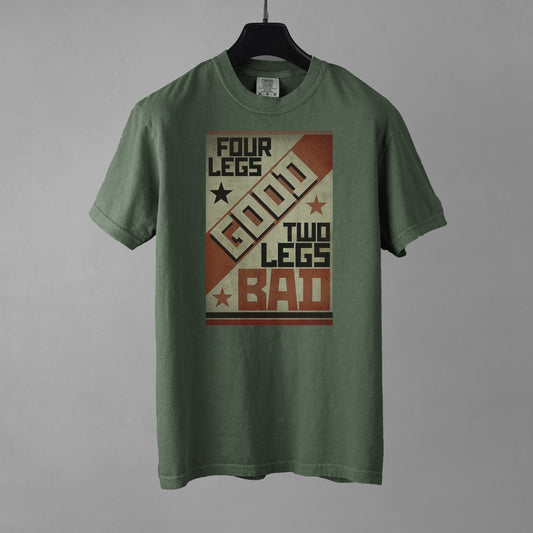 A moss green colored short-sleeve crewneck t-shirt featuring a retro propaganda-style rectangular graphic. The design uses a textured tan, red, and black color palette with diagonal geometric blocking. It features the text 'FOUR LEGS' in black, a large diagonal 'GOOD' in off-white, 'TWO LEGS' in black, and a large 'BAD' in red at the bottom. The design is accented with small black and red stars. The shirt is presented on a black hanger against a gray background.