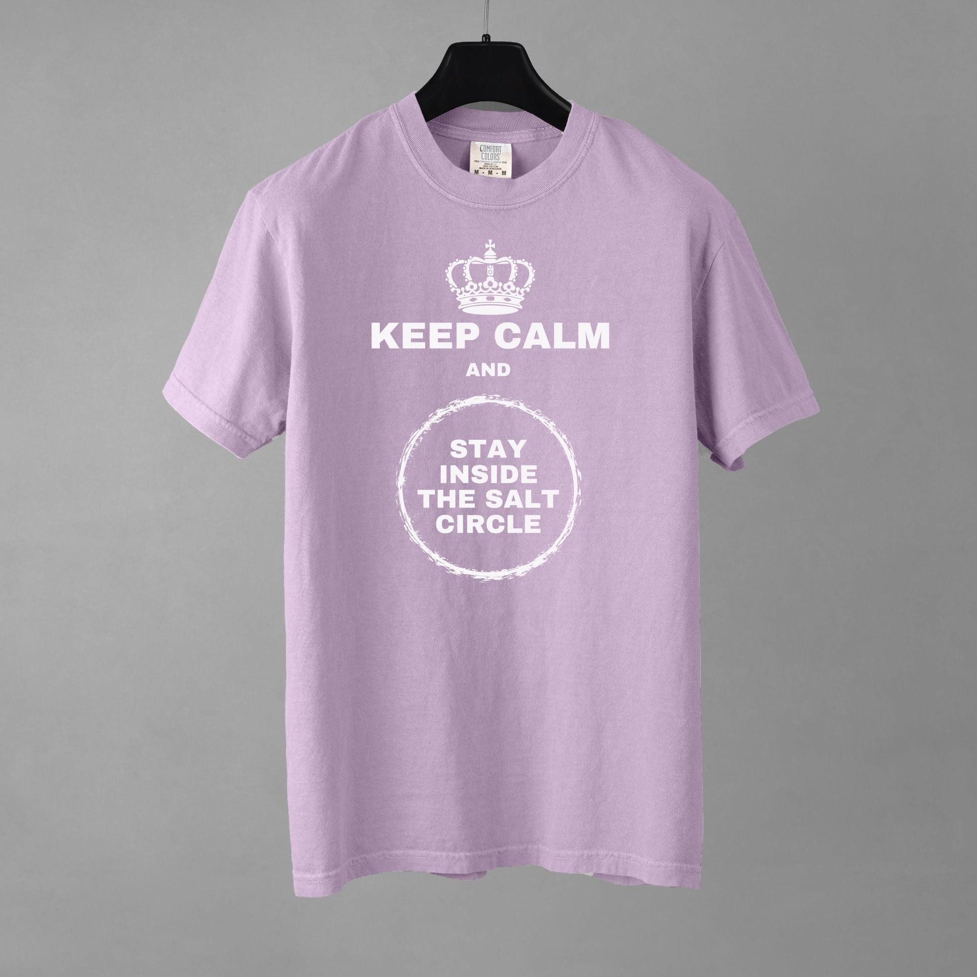 An orchid colored t-shirt with a crown graphic over top of bold all-caps text that reads 'KEEP CALM AND STAY INSIDE THE SALT CIRCLE, with a white circular graphic to represent a 'salt circle'. 