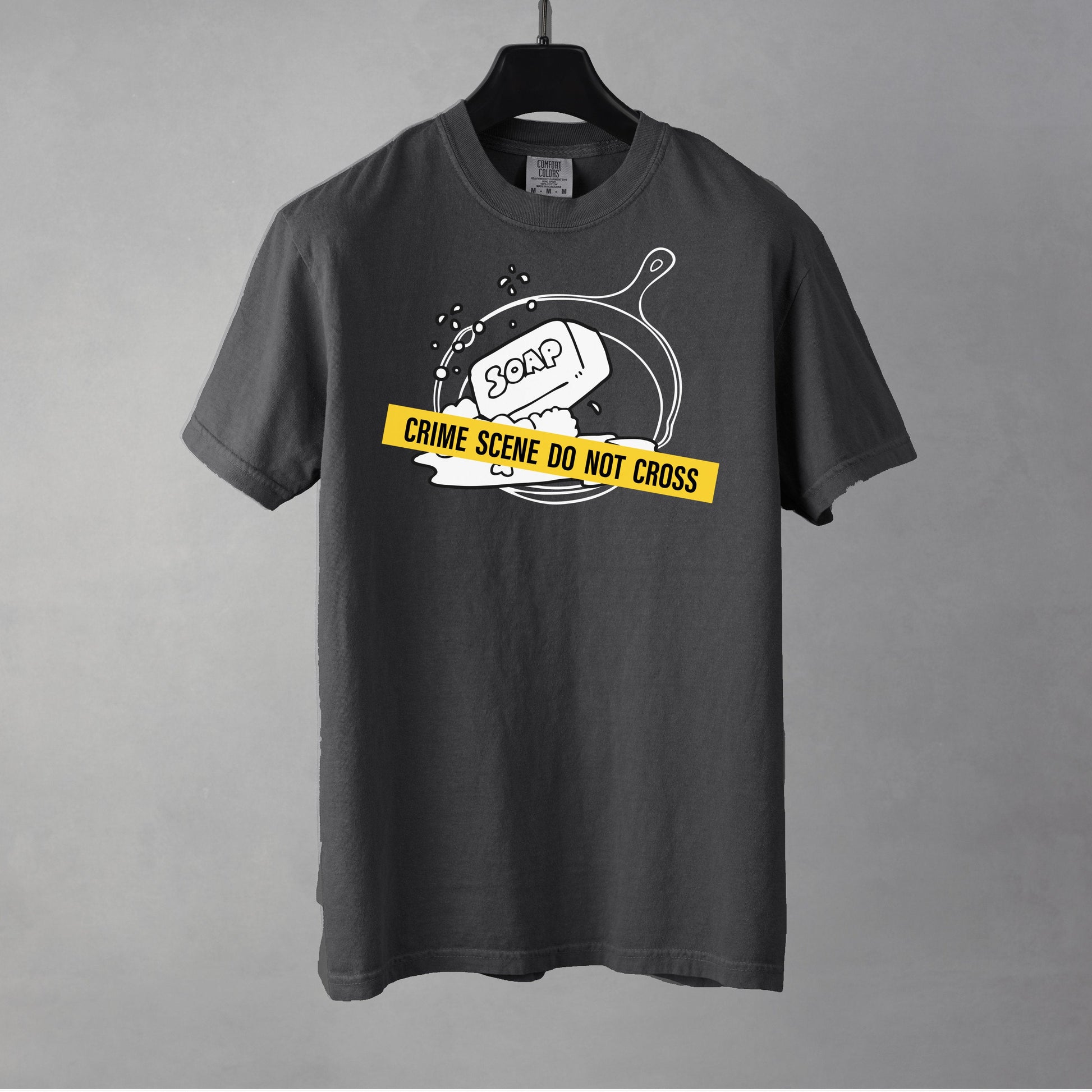 A pepper t-shirt with a graphic of a cast iron pan with a bar of soap in it, crossed with crime scene tape.