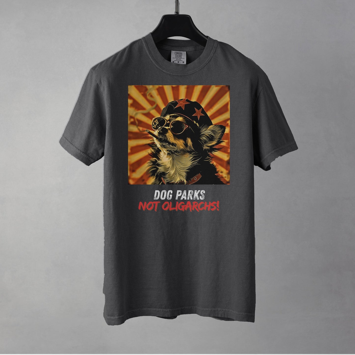 A pepper colored women's t-shirt with a graphic of a Chihuahua wearing sunglasses and a beret against a 50's style propaganda background with bold all-caps text underneath that reads "DOG PARKS NOT OLIGARCHS".