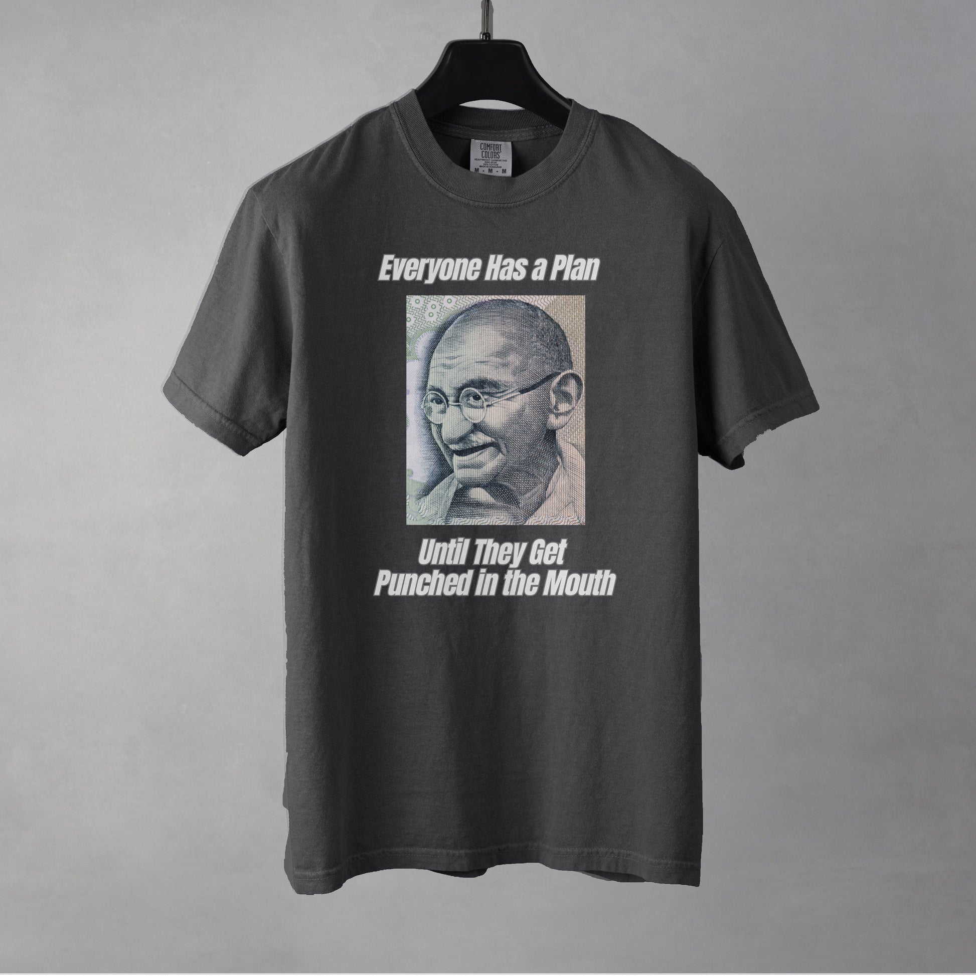 A pepper colored women's graphic t-shirt featuring a vintage portrait of Mahatma Gandhi ironically paired with the famous quote 'Everyone Has a Plan Until They Get Punched in the Mouth'