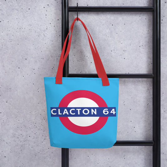A tote bag with a light blue background and red straps. The graphic is a large red, white, and blue target-style roundel with a blue bar reading 'CLACTON 64'.