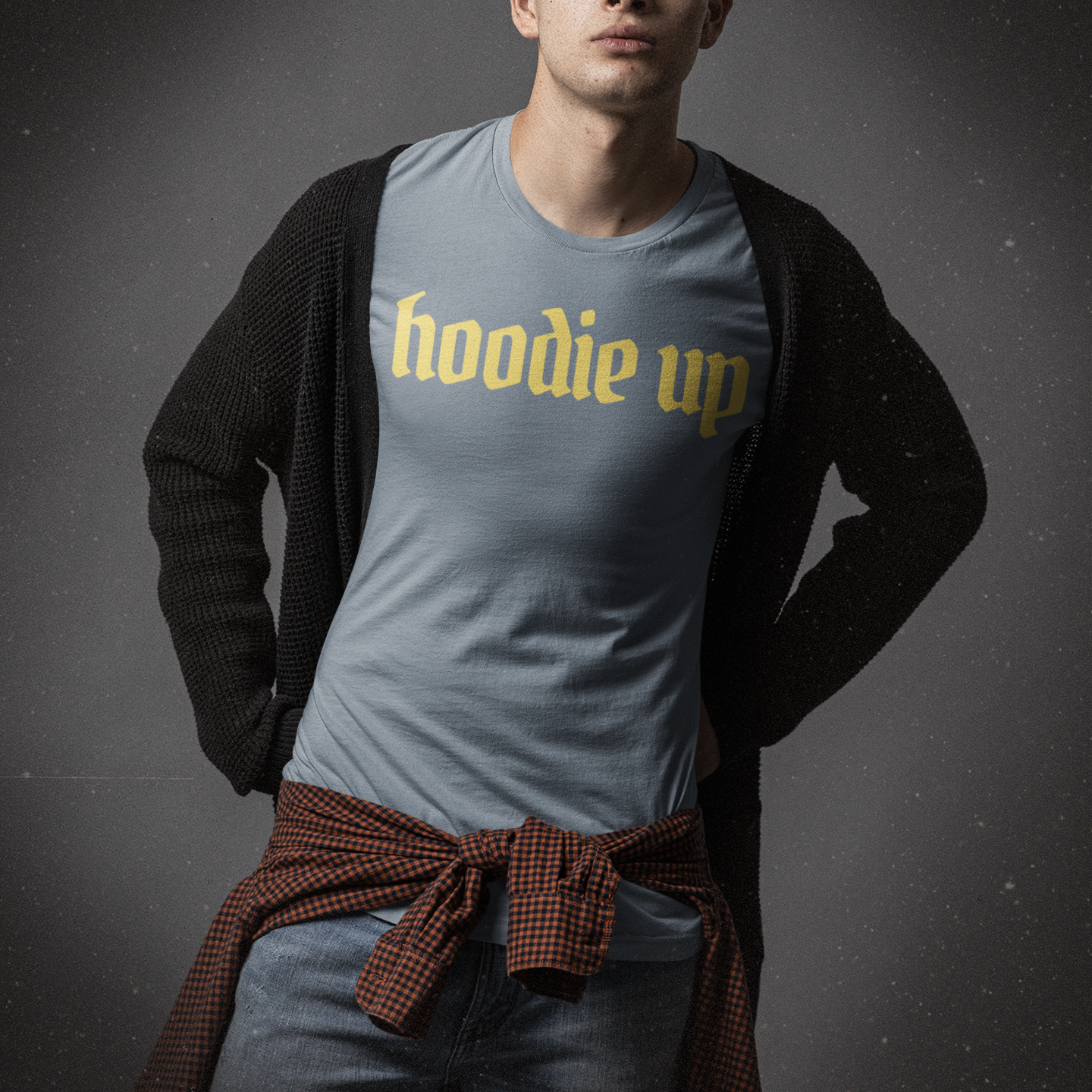 Man wearing a gray t-shirt with 'hoodie up' text and a dark cardigan over his shoulders on a dark background.
