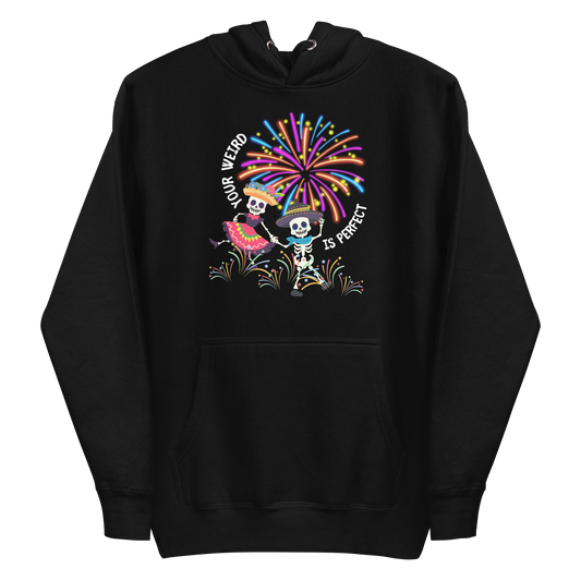 A black premium hoodie featuring a colorful graphic of two skeletons dancing in festive attire under fireworks. Curved text reads 'YOUR WEIRD IS PERFECT'.