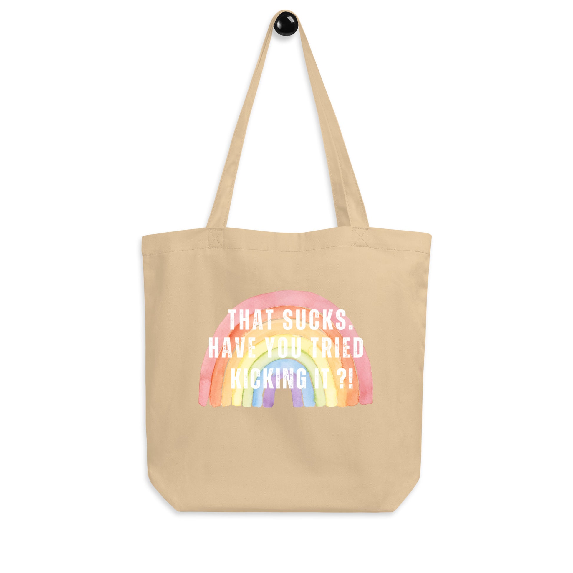 An oyster colored canvas tote bag featuring a pastel watercolor rainbow with the text overlay: 'THAT SUCKS. HAVE YOU TRIED KICKING IT?!'.