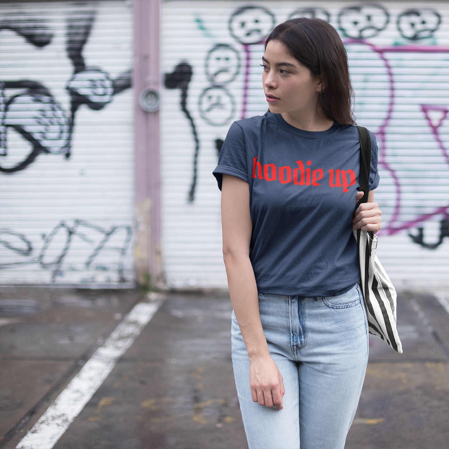 Woman wearing a t-shirt with 'Hoodie up' text in front of a graffiti-covered wall.