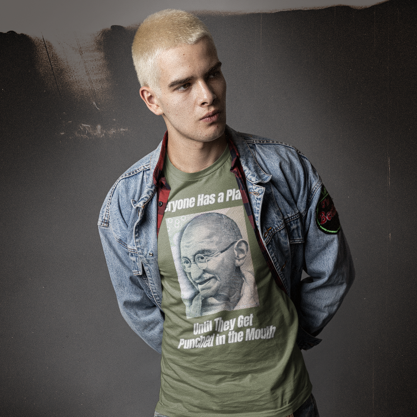 Person wearing a green t-shirt with a graphic design and text, standing against a dark background.