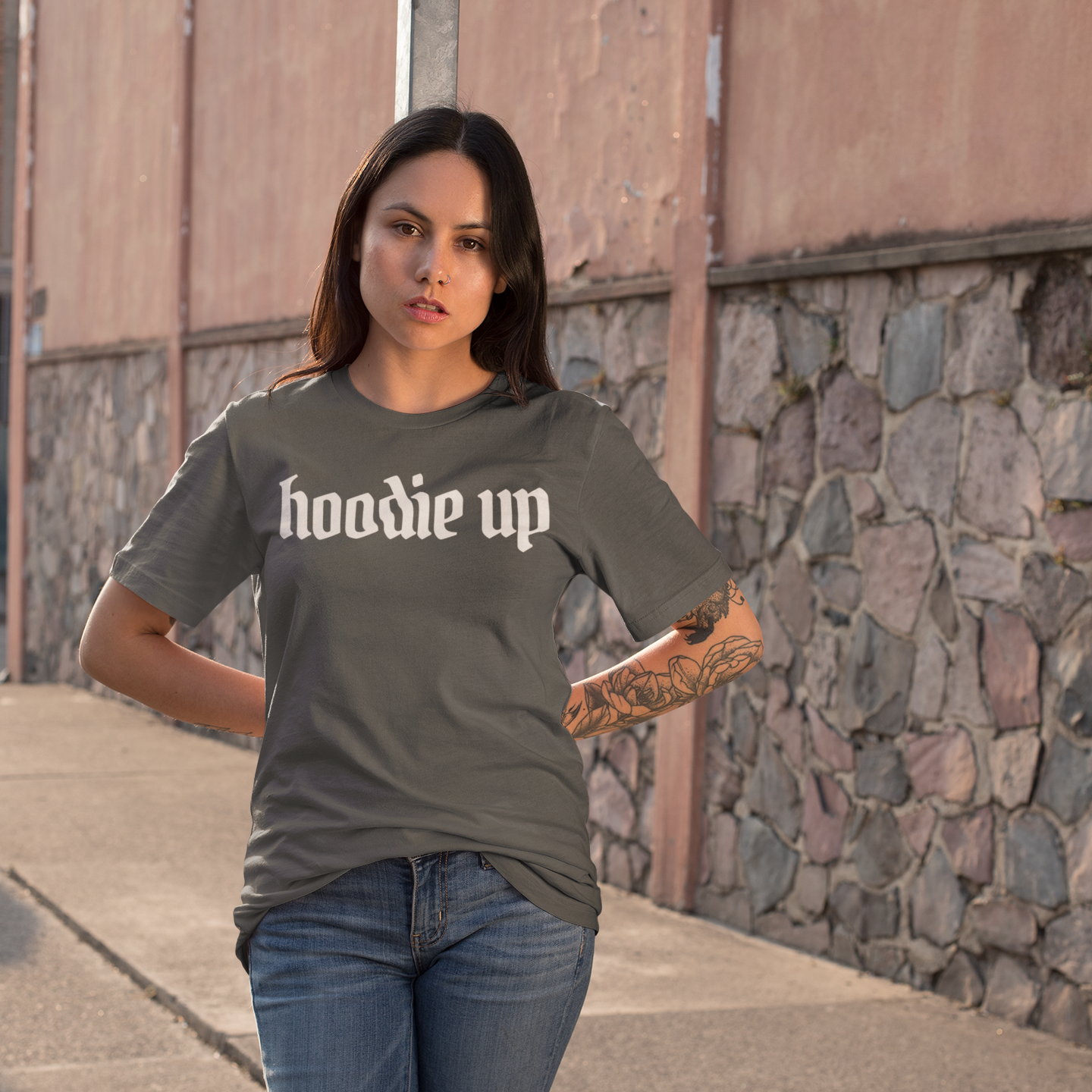 Woman wearing a gray t-shirt with 'hoodie up' text on a stone wall background