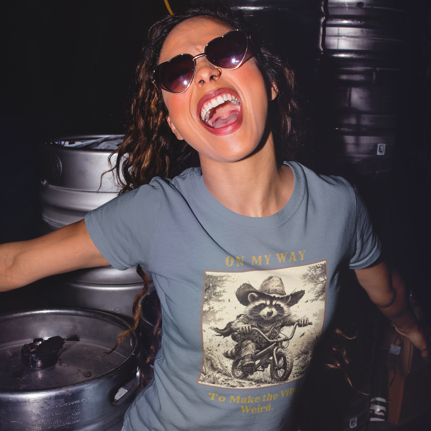 Woman wearing a graphic t-shirt with a cowgirl design in front of metal barrels.