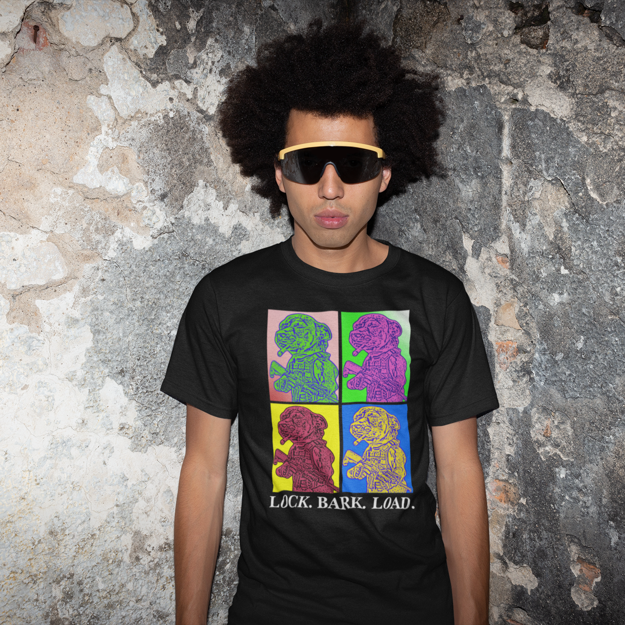 Person wearing a black t-shirt with colorful graphics and text, standing against a textured wall.