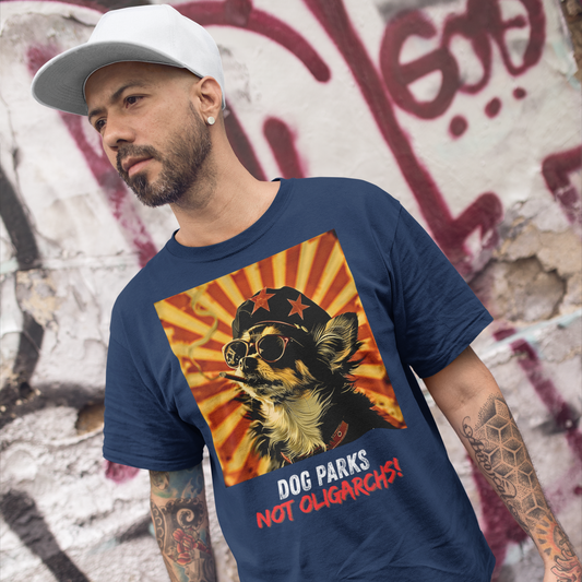 A man with heavily tattooed arms wearing a white dad hat standing in front of a masonry wall covered in graffiti. He is wearing a navy colored men's t-shirt with a graphic of a Chihuahua wearing sunglasses and a beret against a 50's style propaganda background with bold all-caps text underneath that reads "DOG PARKS NOT OLIGARCHS".