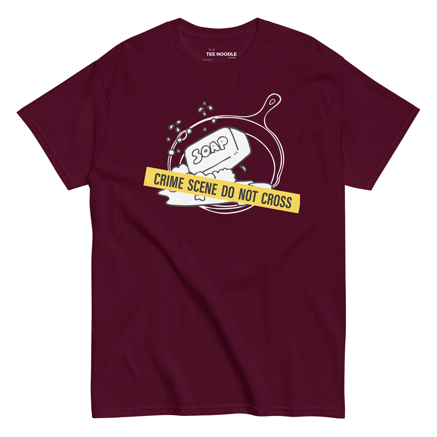 A maroon t-shirt featuring a white line-art graphic of a cast iron skillet filled with bubbles and a bar of soap. A yellow strip of tape across the front reads 'CRIME SCENE DO NOT CROSS'.