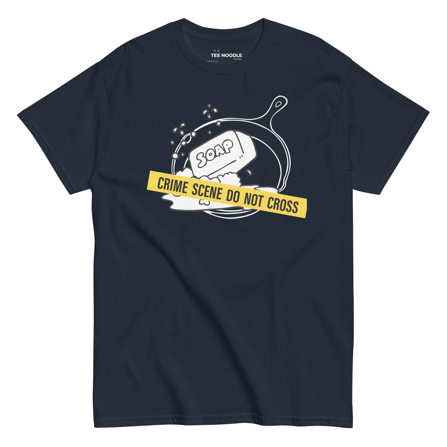 A navy t-shirt featuring a white line-art graphic of a cast iron skillet filled with bubbles and a bar of soap. A yellow strip of tape across the front reads 'CRIME SCENE DO NOT CROSS'.