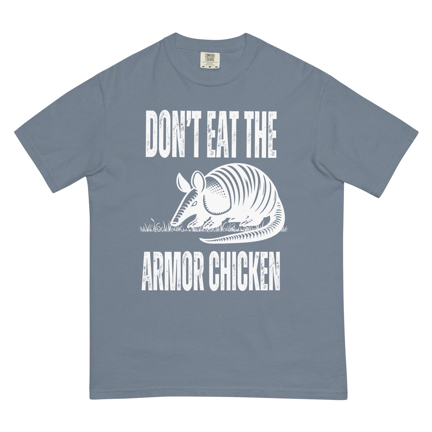 A blue jean colored t-shirt with bold, all-caps, distressed white text that says 'DONT EAT THE ARMOR CHICKEN'. The text is separated into two lines by a white, line drawing graphic of an armadillo eating grass. 