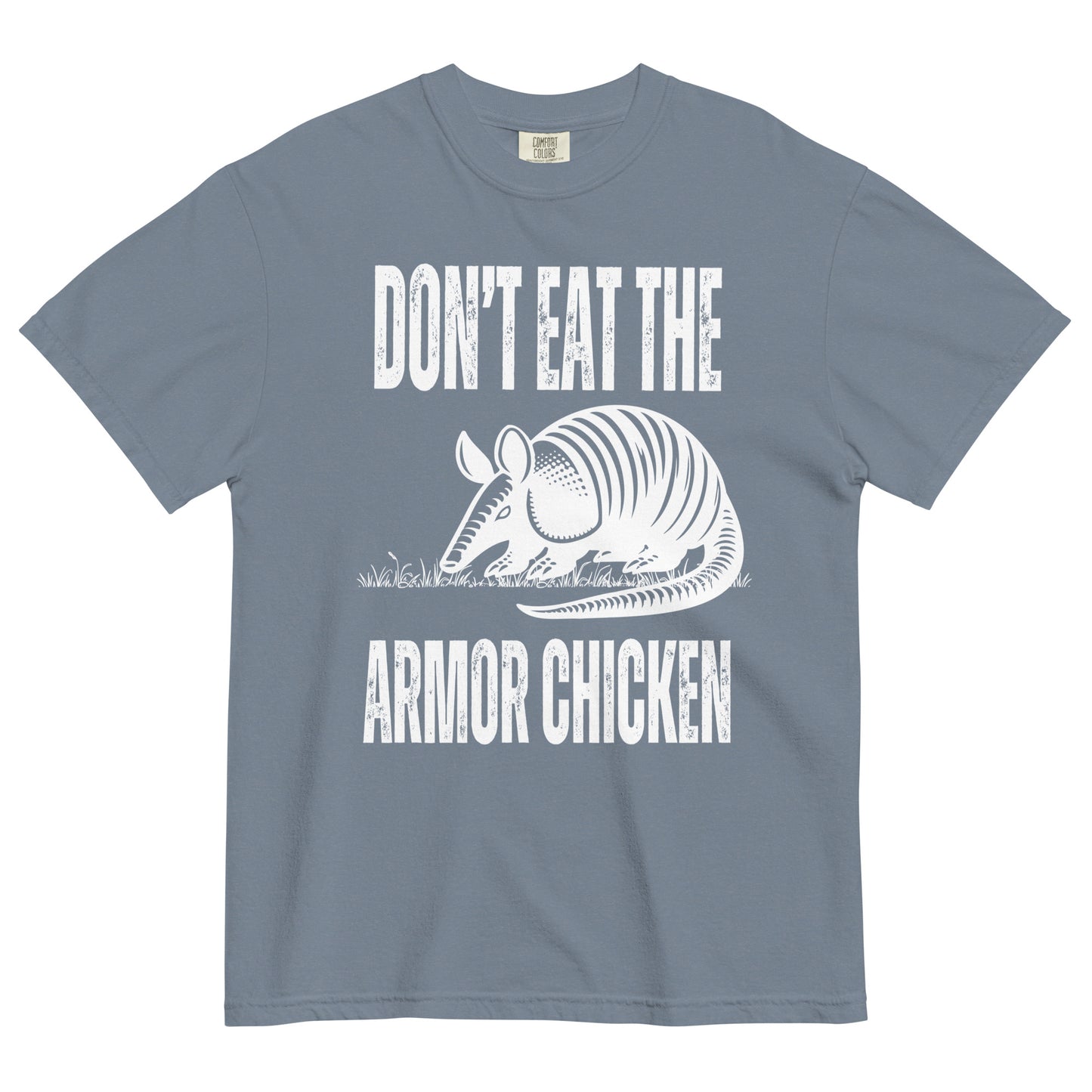 A blue jean colored t-shirt with bold, all-caps, distressed white text that says 'DONT EAT THE ARMOR CHICKEN'. The text is separated into two lines by a white, line drawing graphic of an armadillo eating grass. 