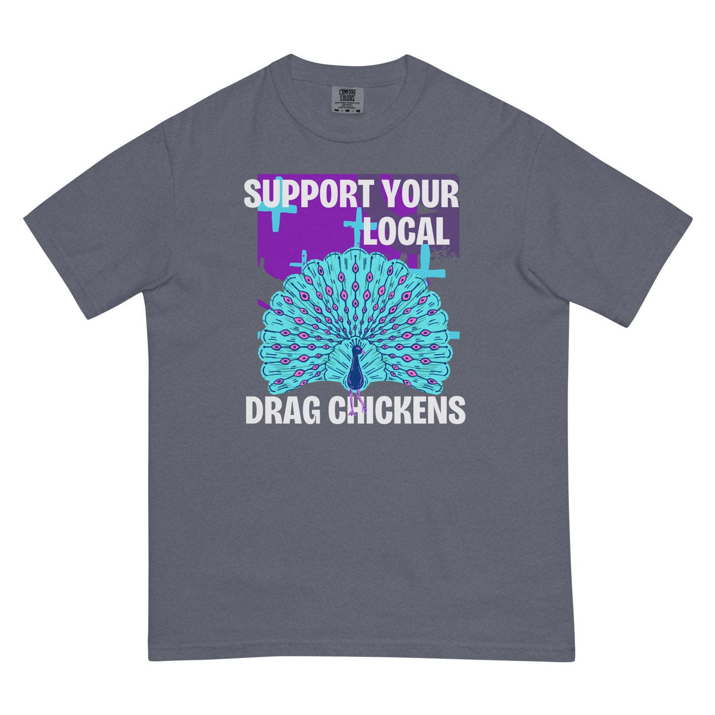 A denim colored short-sleeve crewneck t-shirt featuring a stylized graphic of a peacock with its tail feathers fully fanned out. The peacock is light blue with pink eye details, set against a distressed purple background block with light blue plus signs. Above the peacock is bold white text reading 'SUPPORT YOUR LOCAL', and below it reads 'DRAG CHICKENS'.