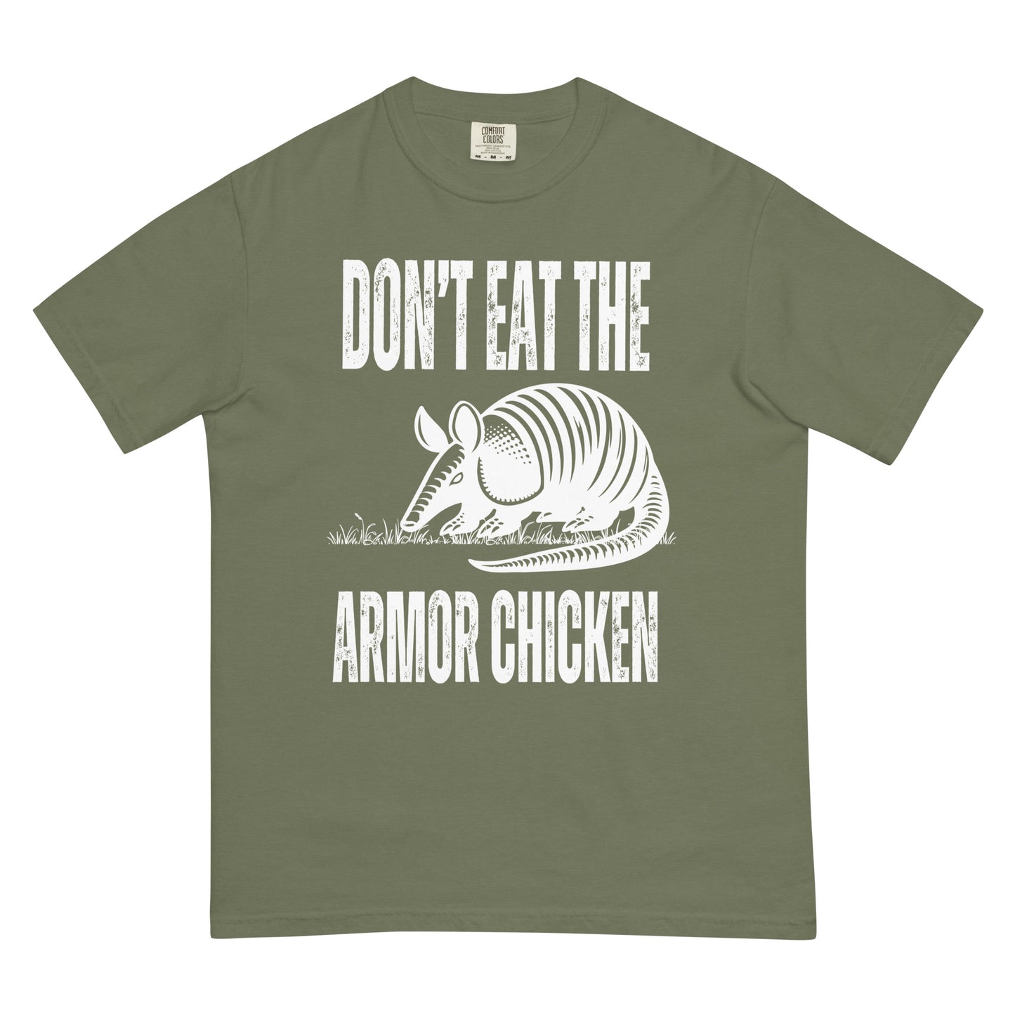 A moss green colored t-shirt with bold, all-caps, distressed white text that says 'DONT EAT THE ARMOR CHICKEN'. The text is separated into two lines by a white, line drawing graphic of an armadillo eating grass. 