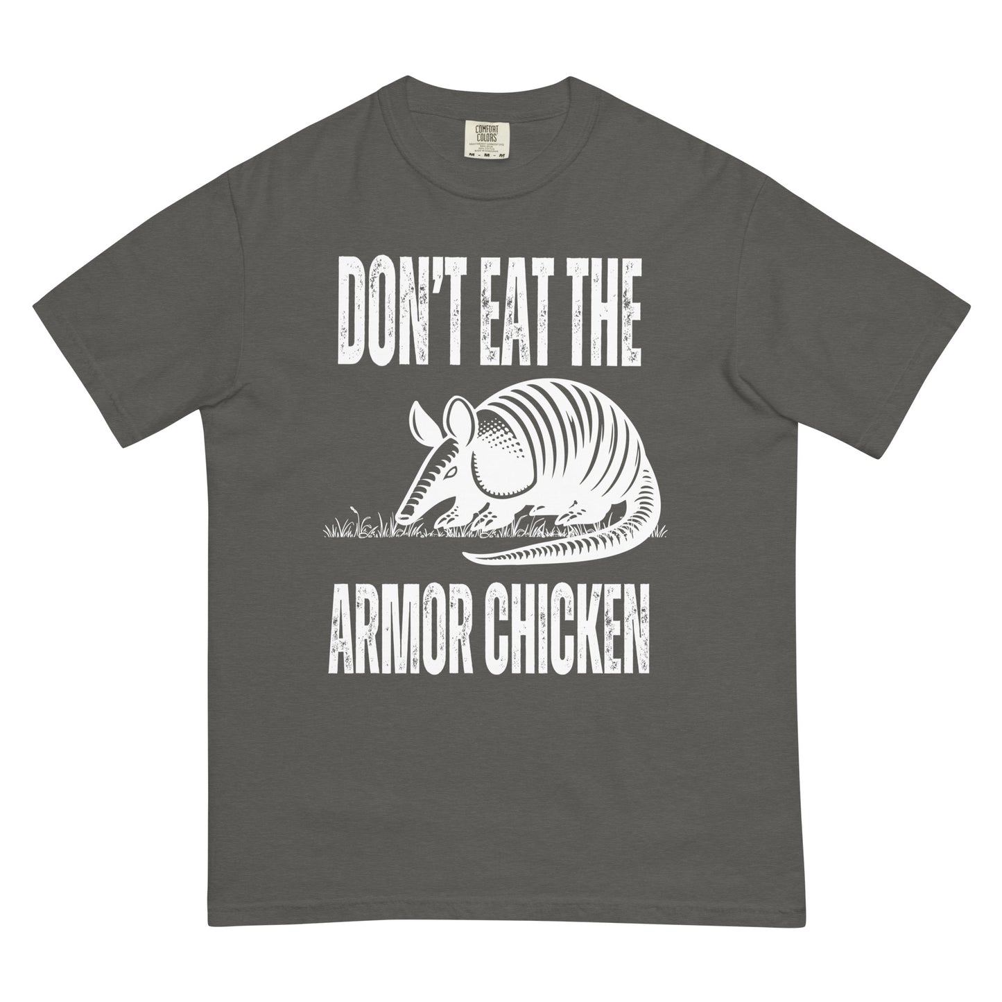 A pepper colored t-shirt with bold, all-caps, distressed white text that says 'DONT EAT THE ARMOR CHICKEN'. The text is separated into two lines by a white, line drawing graphic of an armadillo eating grass. 